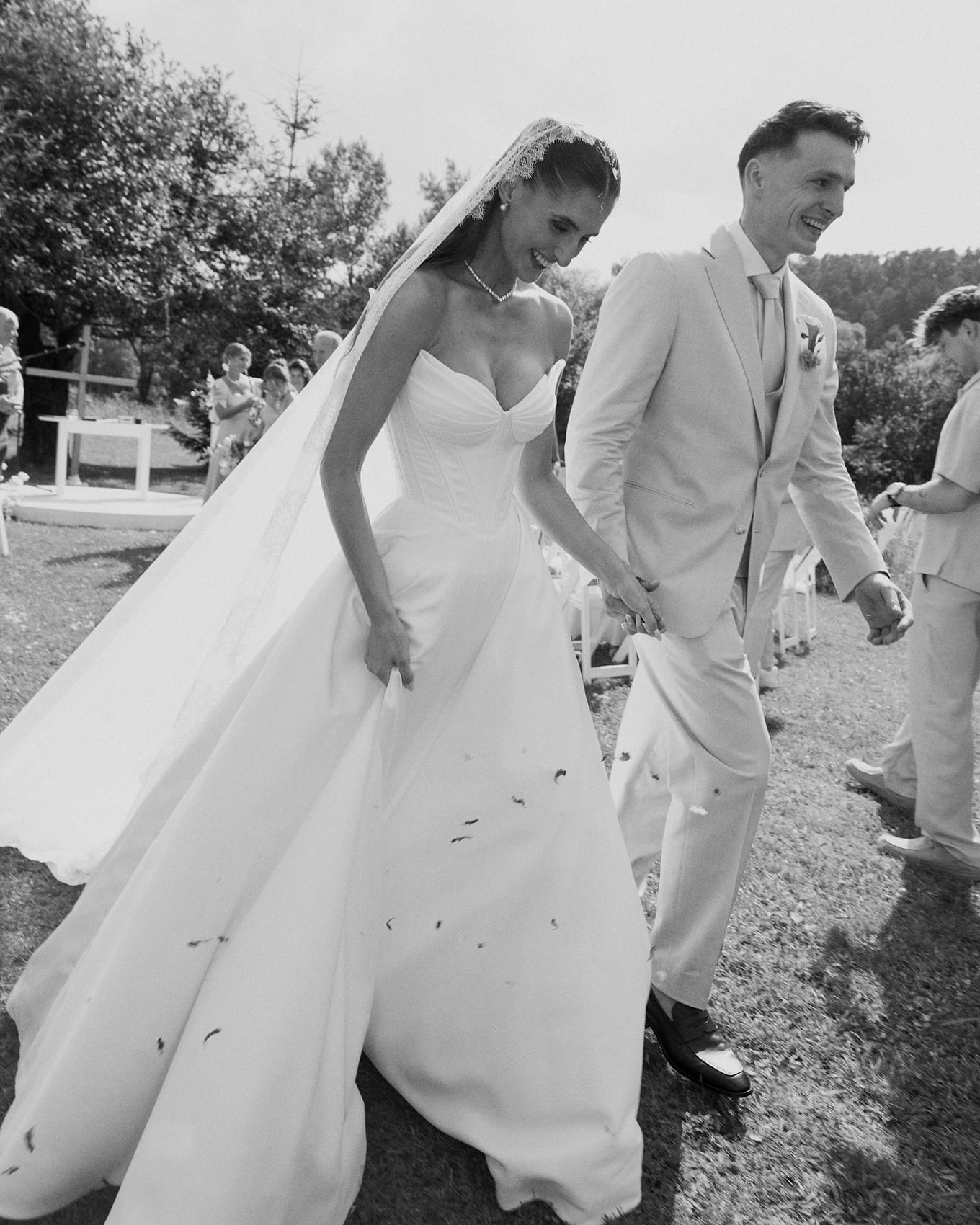 Newlyweds smiling as petals fall around them while they walk across the lawn after the ceremony