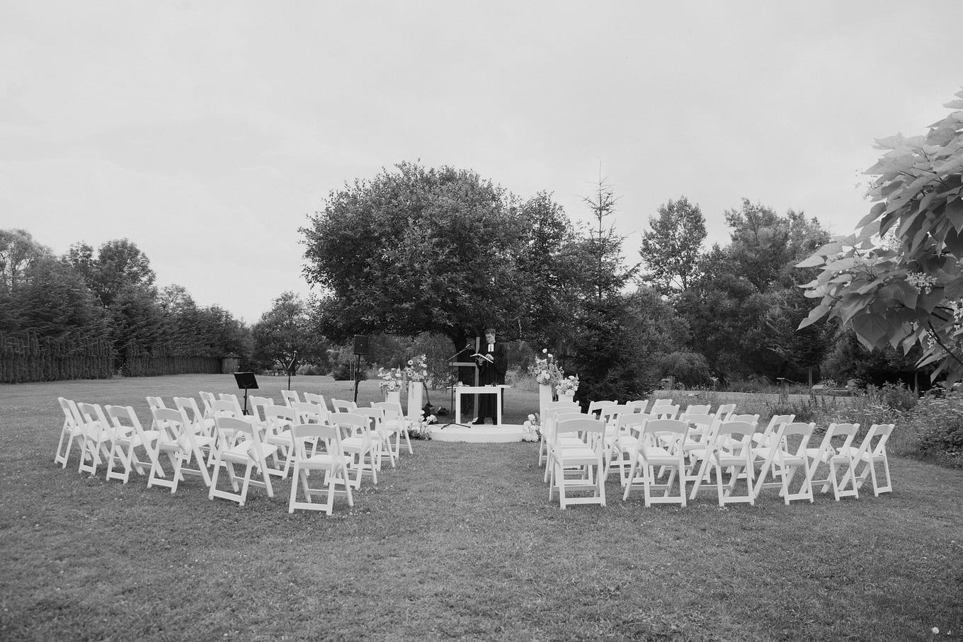 Empty white folding chairs arranged in curved rows on a lawn facing a small outdoor altar