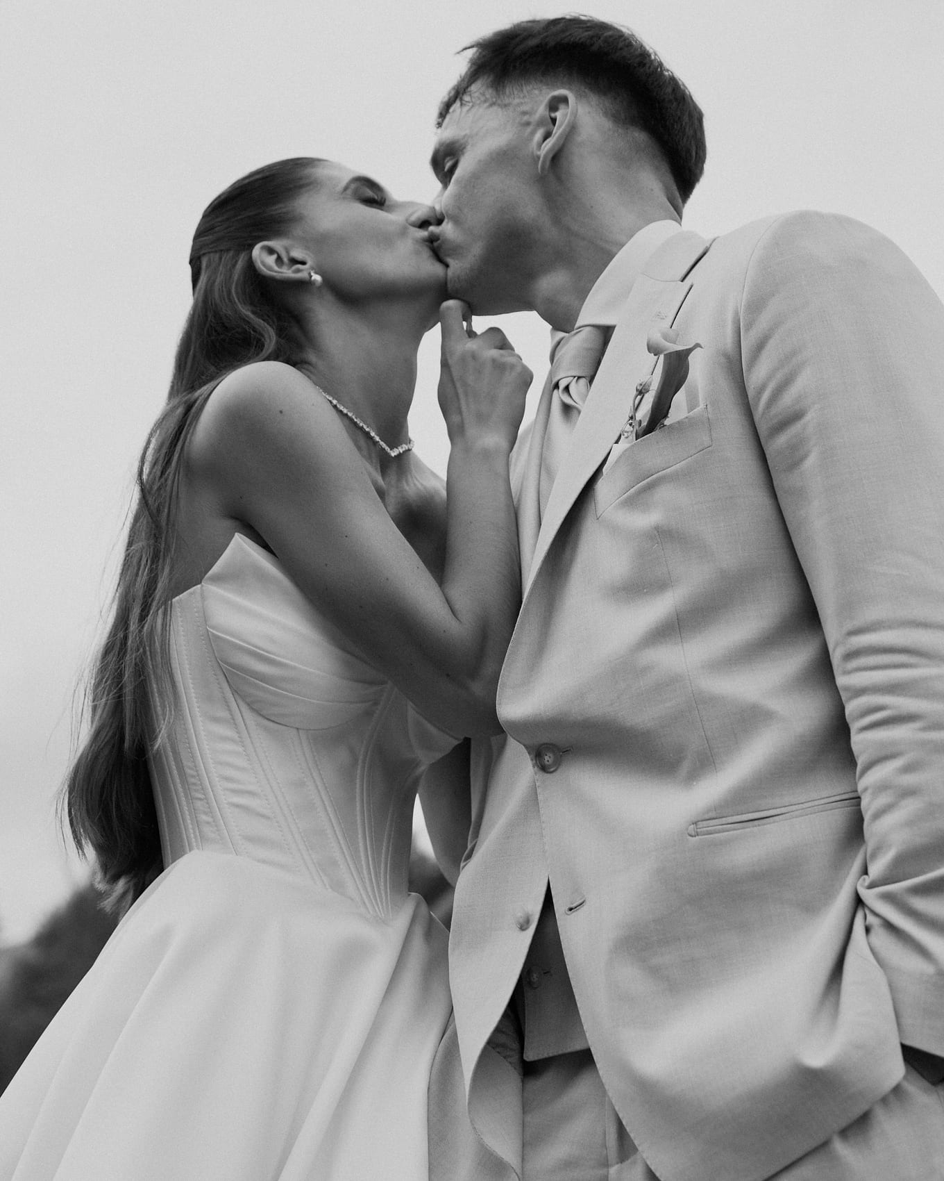 Black-and-white low-angle shot of a bride and groom kissing, her hand resting at his chin