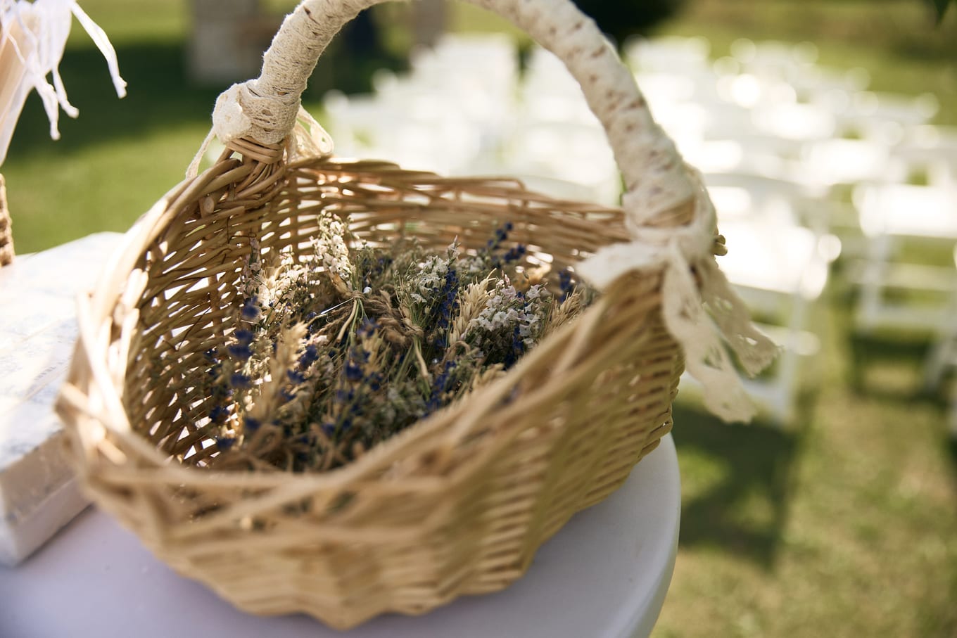 Wicker basket of dried lavender on a white table, rows of white chairs blurred on the lawn behind
