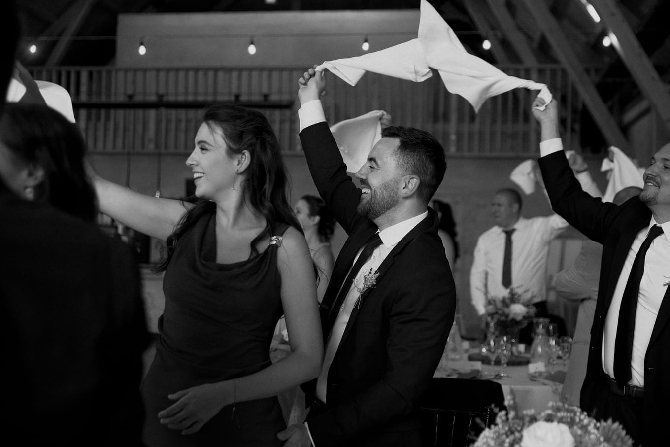 Smiling woman in a dark dress beside a bearded man spinning a napkin over his head
