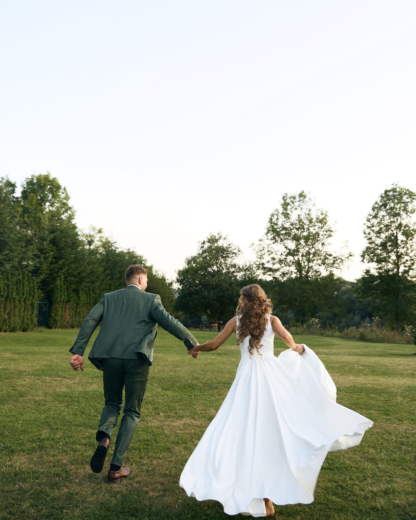 Hand in hand, the couple runs across a lawn toward the trees, her long white skirt swinging out