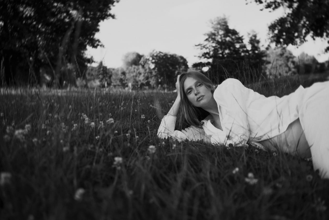 In a field of clover, a woman in a white shirt reclines on one elbow with a hand in her hair