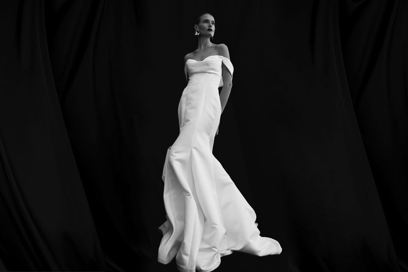 Model crossing a dark studio in a satin gown, the train catching the light