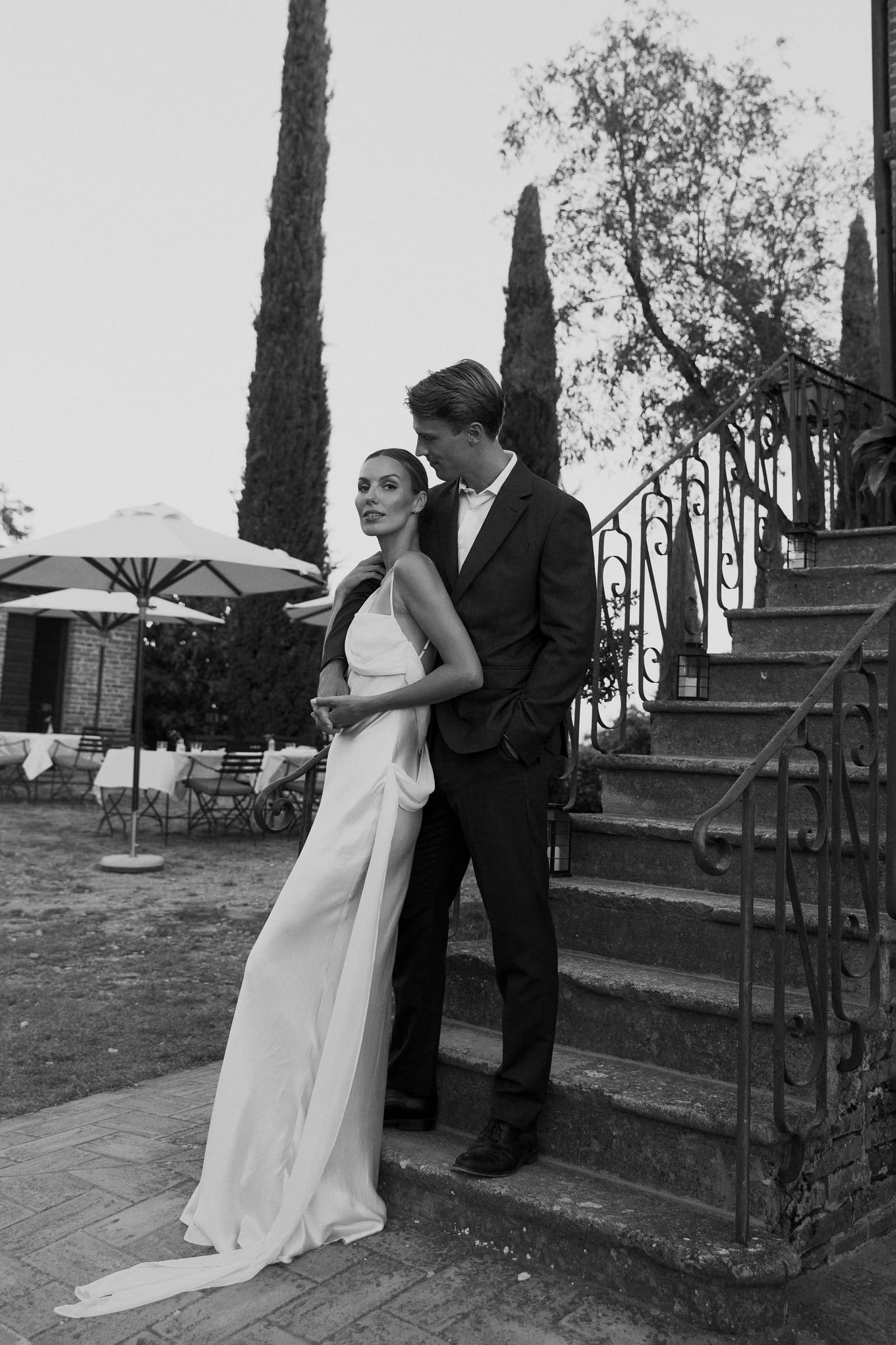 Groom holds the bride from behind at the base of stone steps as she looks toward the camera