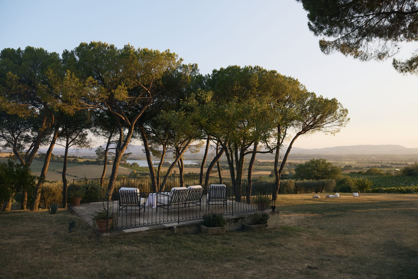 Wrought-iron chairs on a stone terrace beneath umbrella pines overlooking a valley at dusk