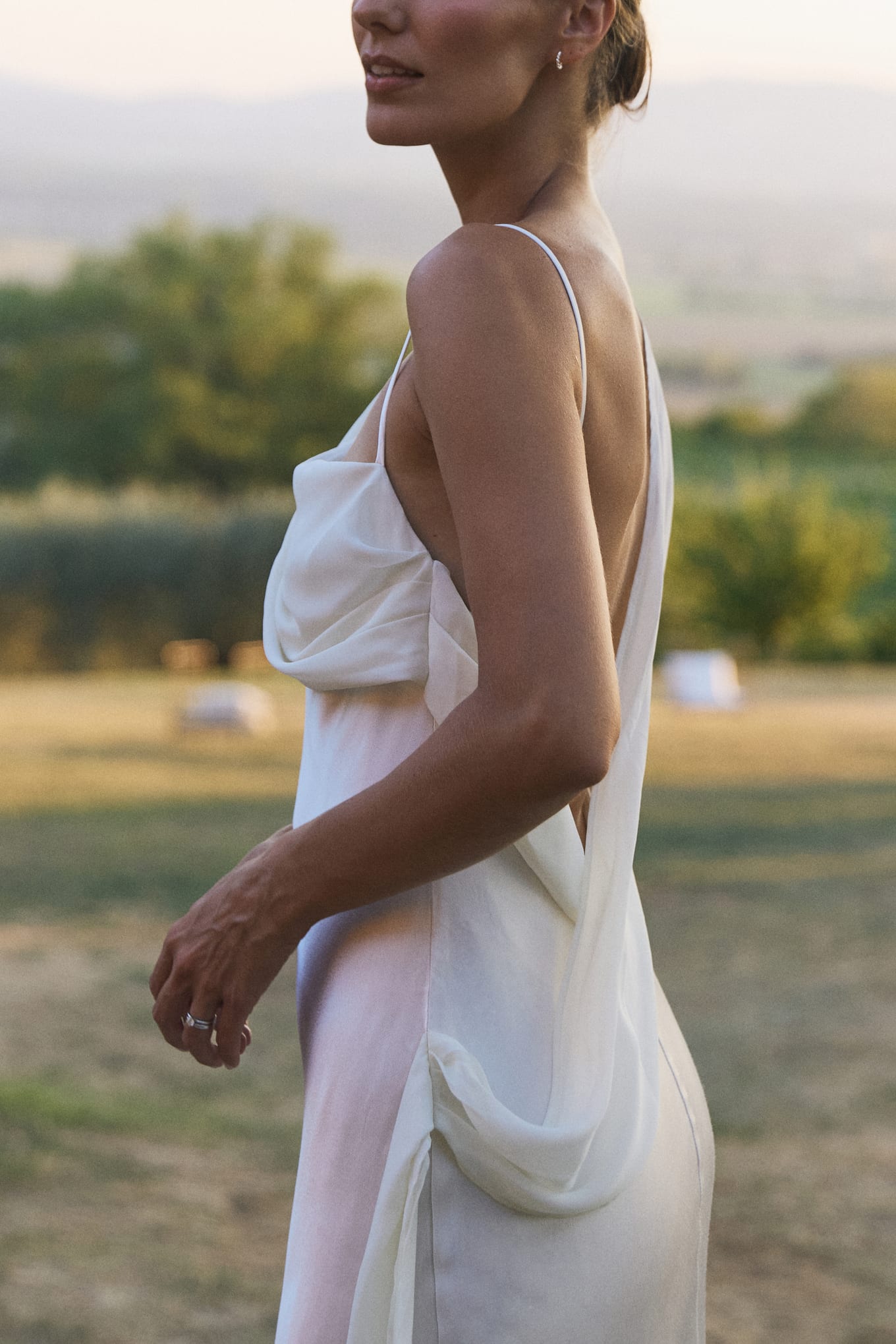 Side view of a bride in a white slip dress with a draped open back, hand resting at her waist