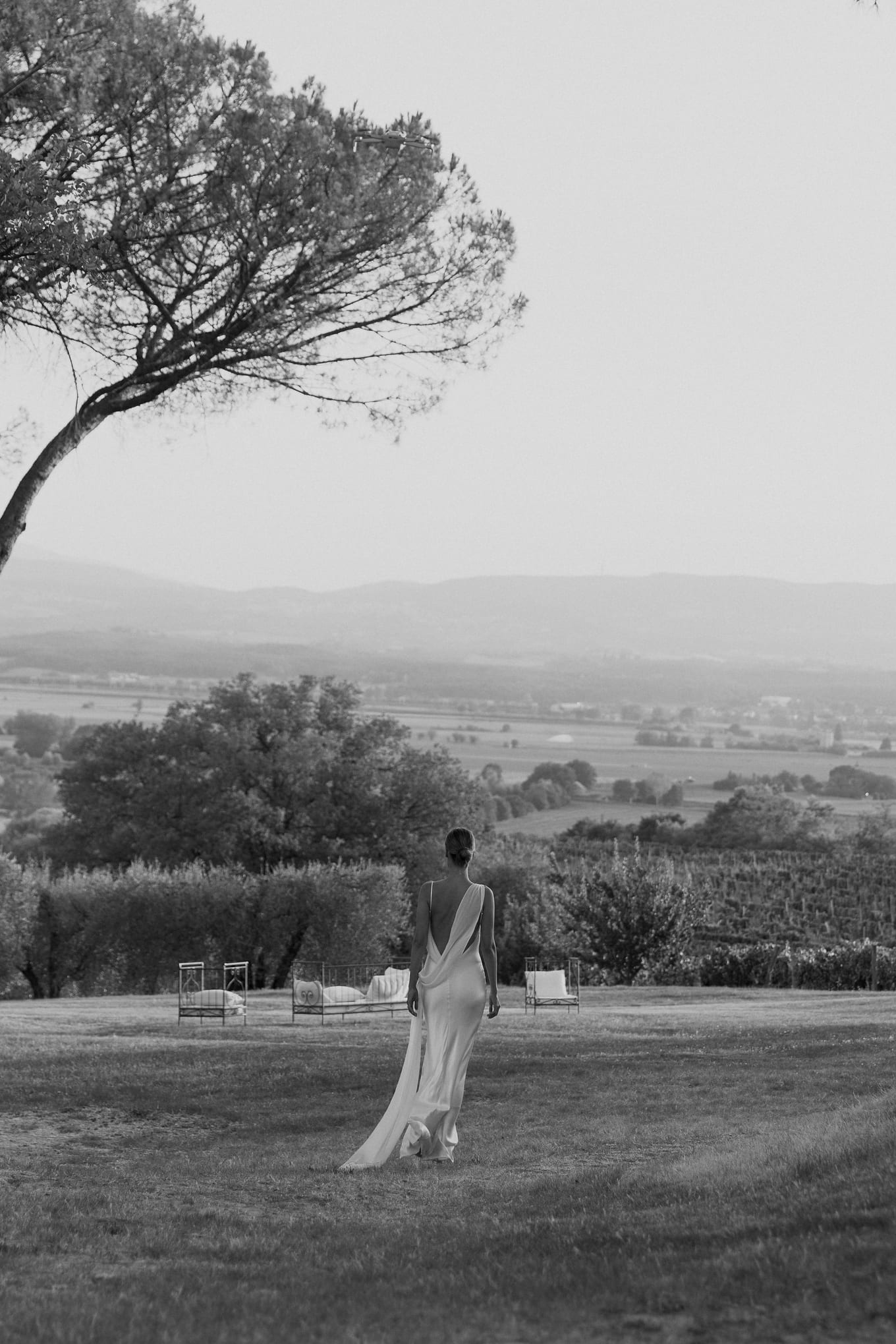 Walking away down the lawn toward vineyards, a bride's long train follows her in black and white