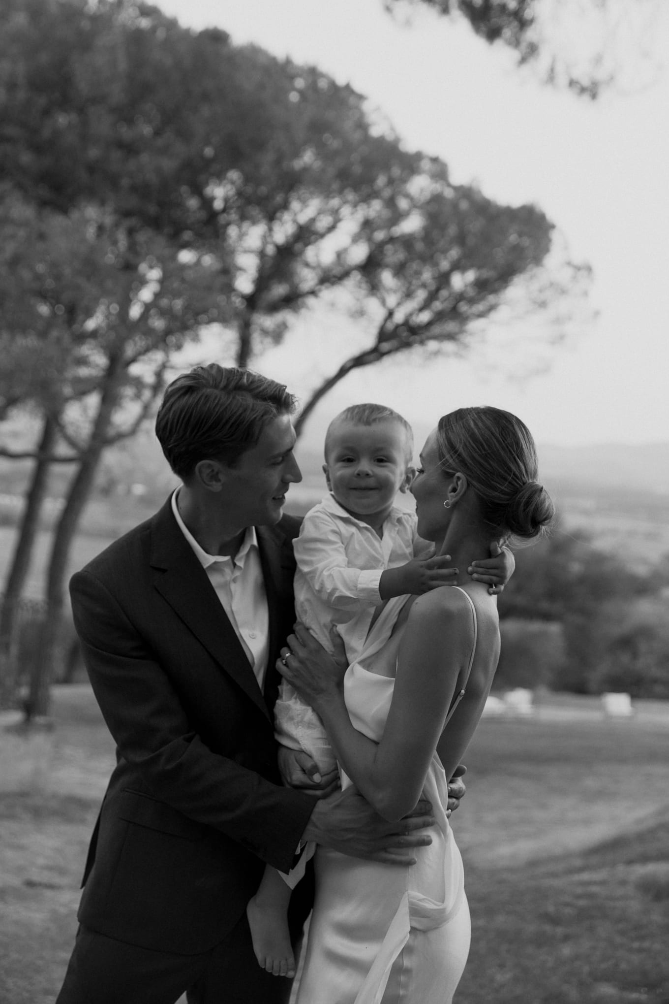 In black and white, a toddler held between a man and a woman smiles as they both turn their faces to him