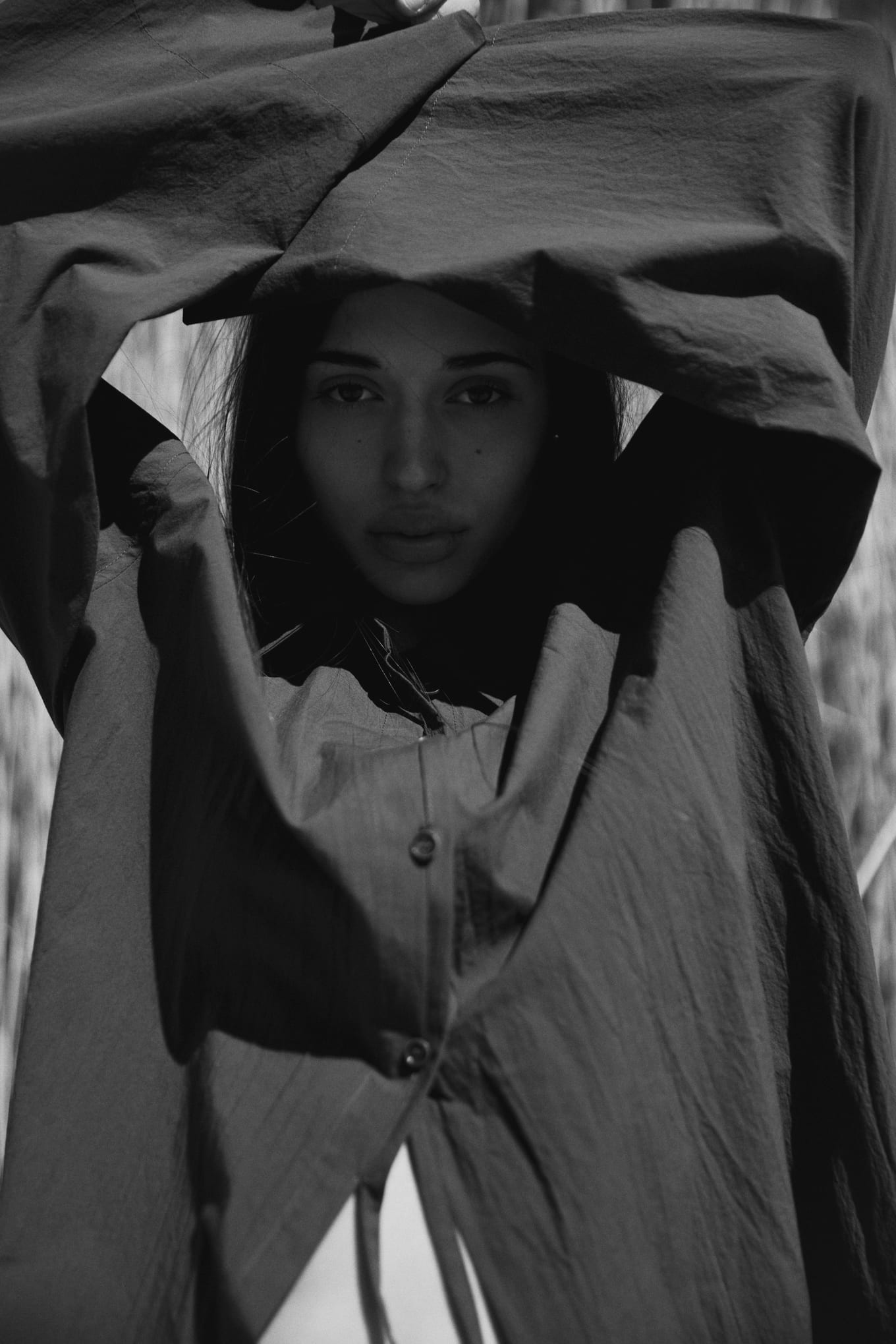 Woman with arms raised overhead, wrapped in a large dark crinkled shirt that frames her face