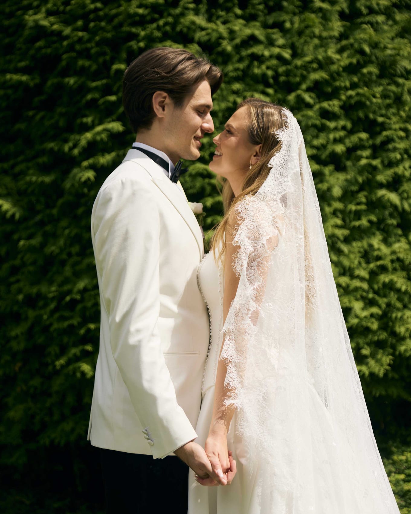 Bride and groom hand in hand against a wall of ivy