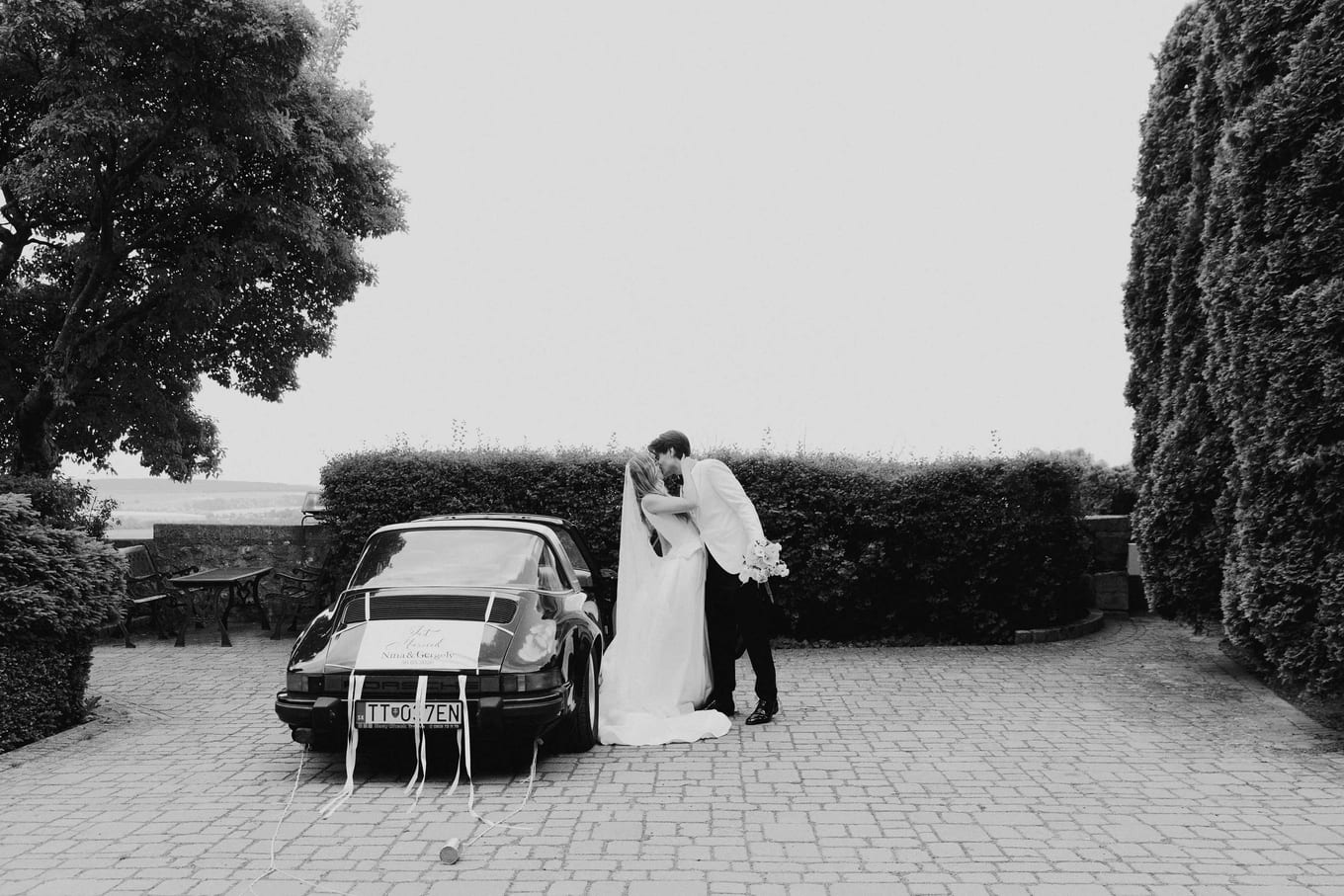 The couple beside the car in front of the hedges